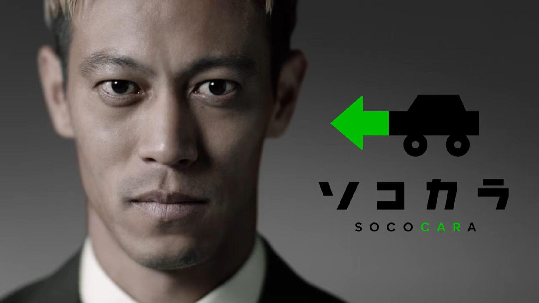 スクリーンショット 2026-07-31 111247 | 車買取のソコカラ Close-up portrait of a man in a suit on the left, with a green arrow logo and the word SOCOCARA on a gray background.