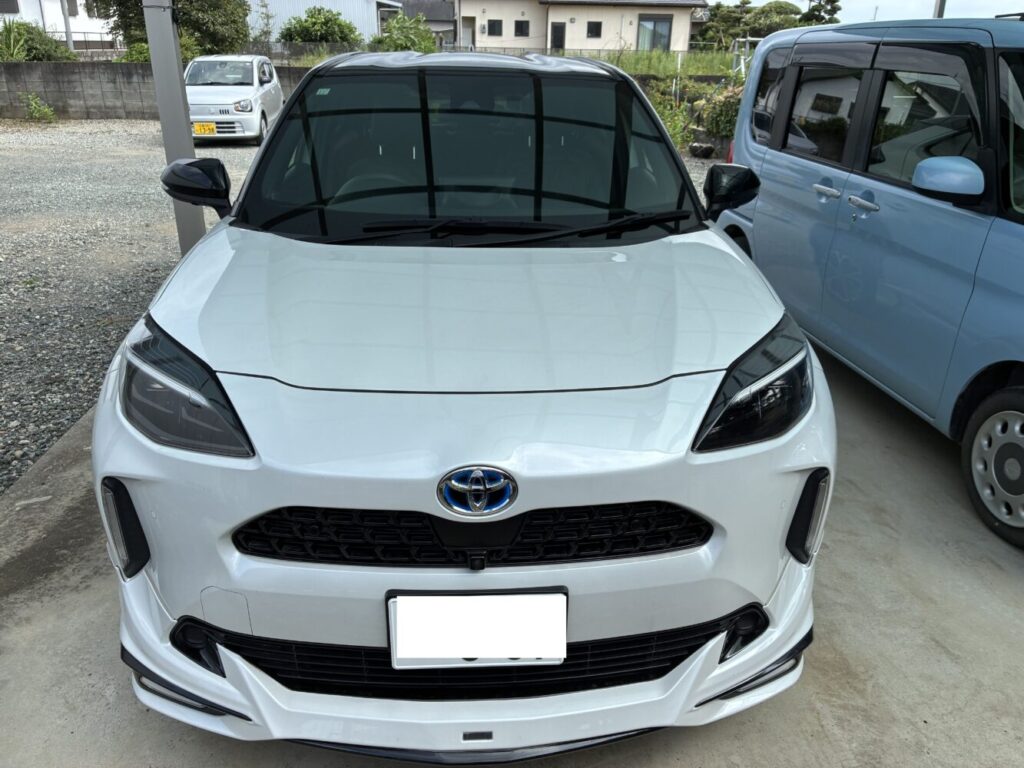 Front view of a white Toyota SUV parked in a lot, with a blue car beside it and a small white car in the background under a covered area