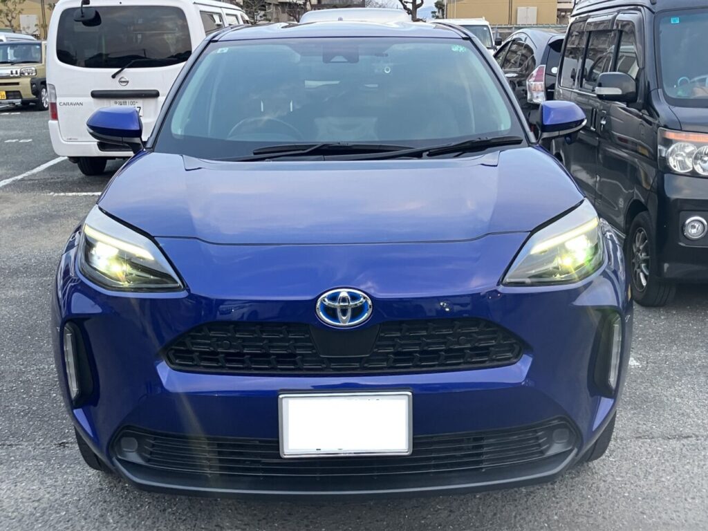 Front view of a blue Toyota SUV with headlights on, parked in a crowded parking lot.