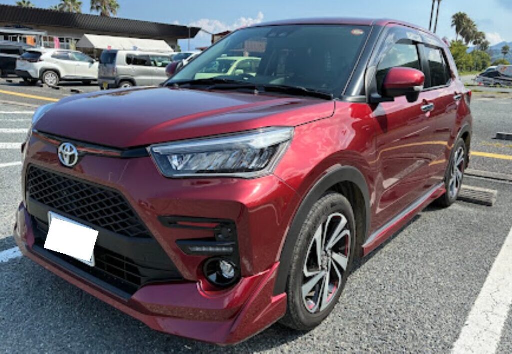 ライズ事例 | 車買取のソコカラ Red Toyota SUV parked in a lot, front-left angle, daytime with other cars in background.