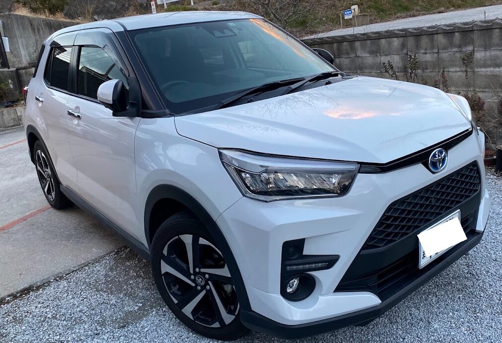 ライズ事例_白 | 車買取のソコカラ White Toyota SUV parked on gravel, front three-quarter view with black grille and angular headlights.",
