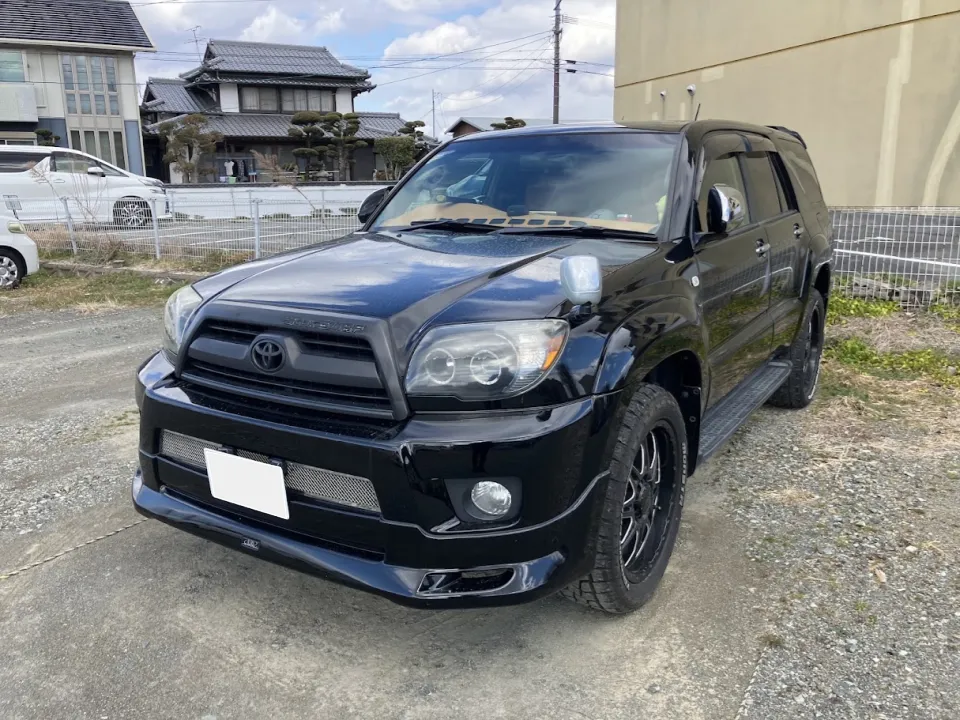Black Toyota SUV parked on a gravel lot; front three-quarter view with houses and a fence in the background.