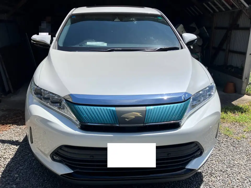Front view of a white SUV parked on gravel, with a teal-accented grille and a front license plate area blanked out for privacy