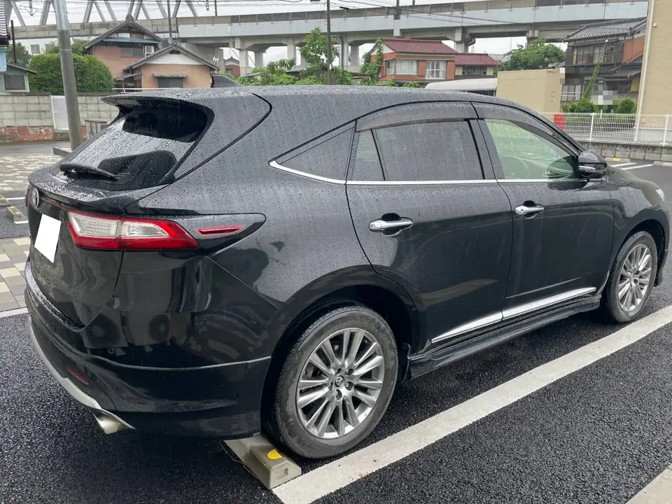 Black SUV parked in a rain-soaked parking lot, rear three-quarter view with chrome window trim, alloy wheels, roof spoiler, and a white license plate.