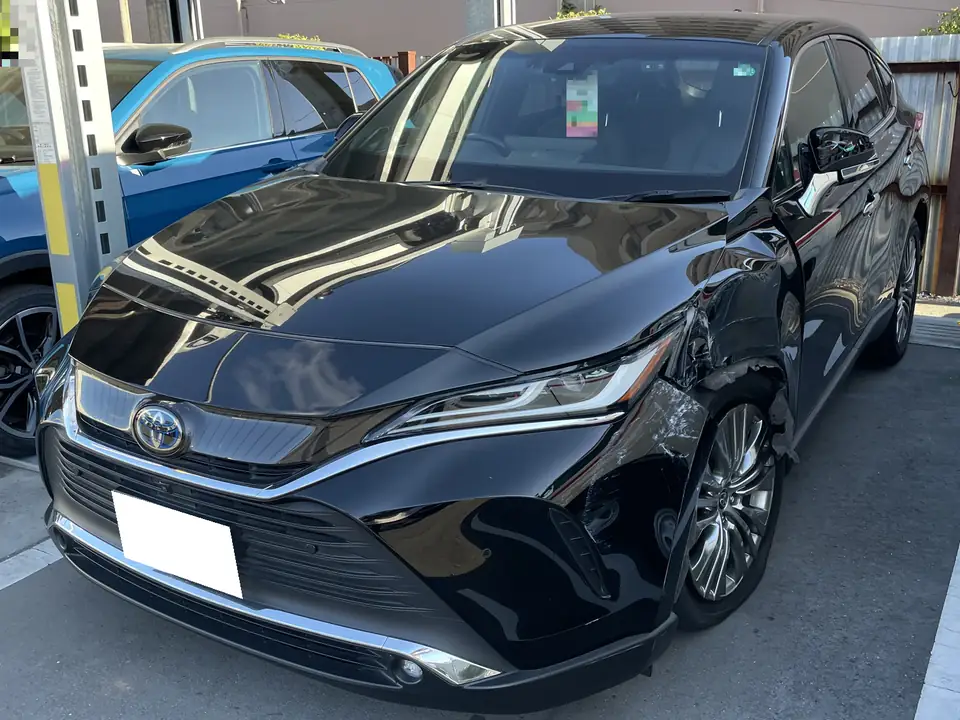 Black Toyota sedan with front-right damage, parked in a lot beside a blue car, showing dented fender and wheel area.